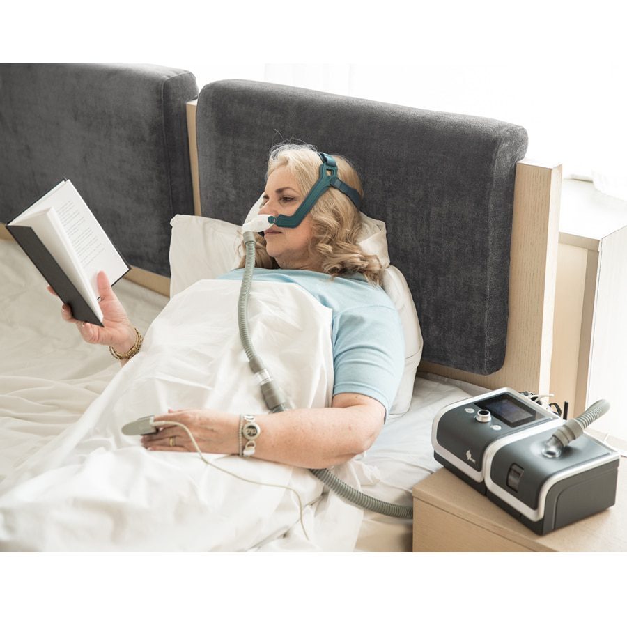 Woman reading in bed while using the Automatic CPAP Machine E-20AJ